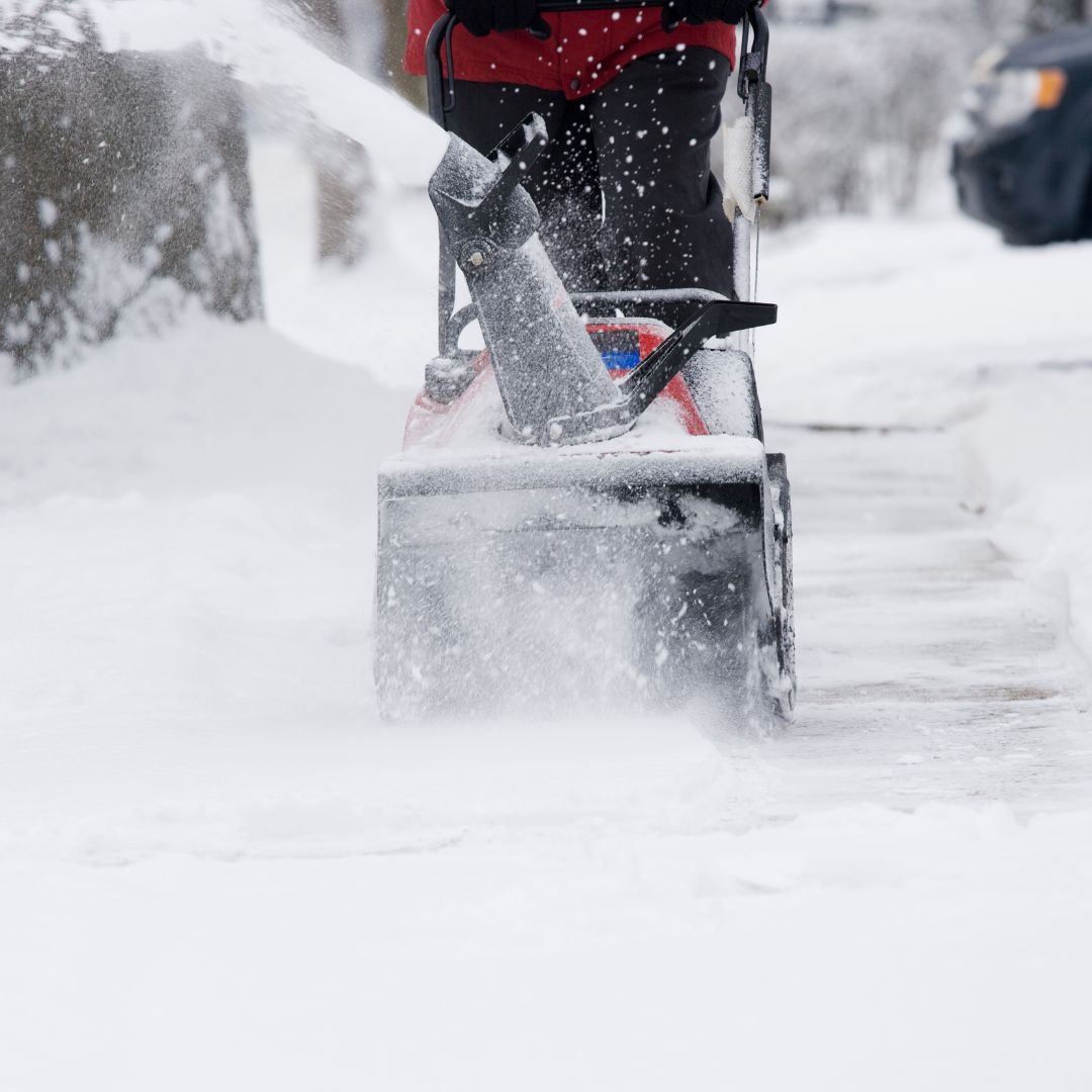 Person using a snowblower on a snowy sidewalk, blowing snow away.