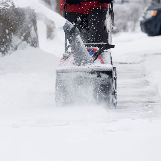 Person using a snowblower on a snowy sidewalk, blowing snow away.