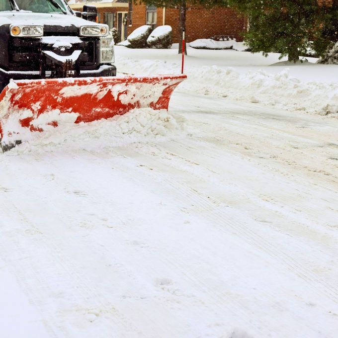 Snowplow clearing a snow-covered road. Red plow blade, white snow, and a truck.