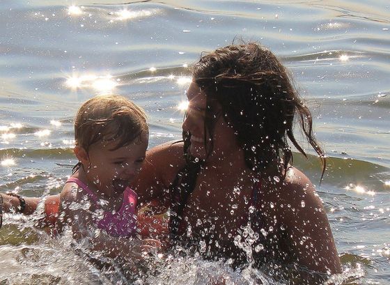 Adult and child splashing in the water, smiling in bright sunlight