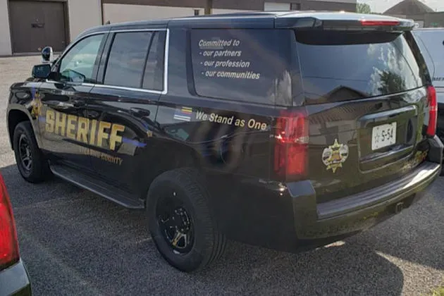 A black SUV marked "SHERIFF" parked outside, featuring the phrase "We Stand as One" on its rear side window.