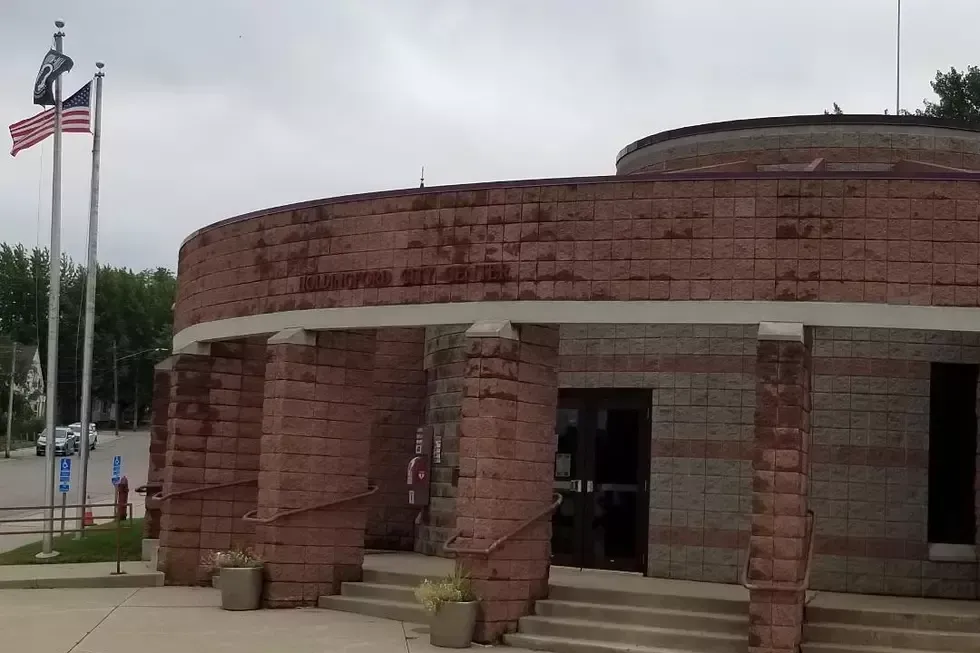 A circular municipal civic center building made of reddish-brown stone blocks with flagpoles and stairs in front.