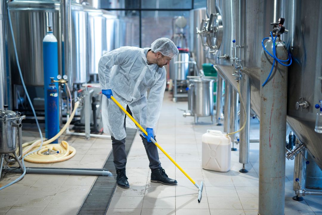 Un operaio con indumenti protettivi pulisce con idropulitrice il pavimento in acciaio inossidabile di uno stabilimento industriale.