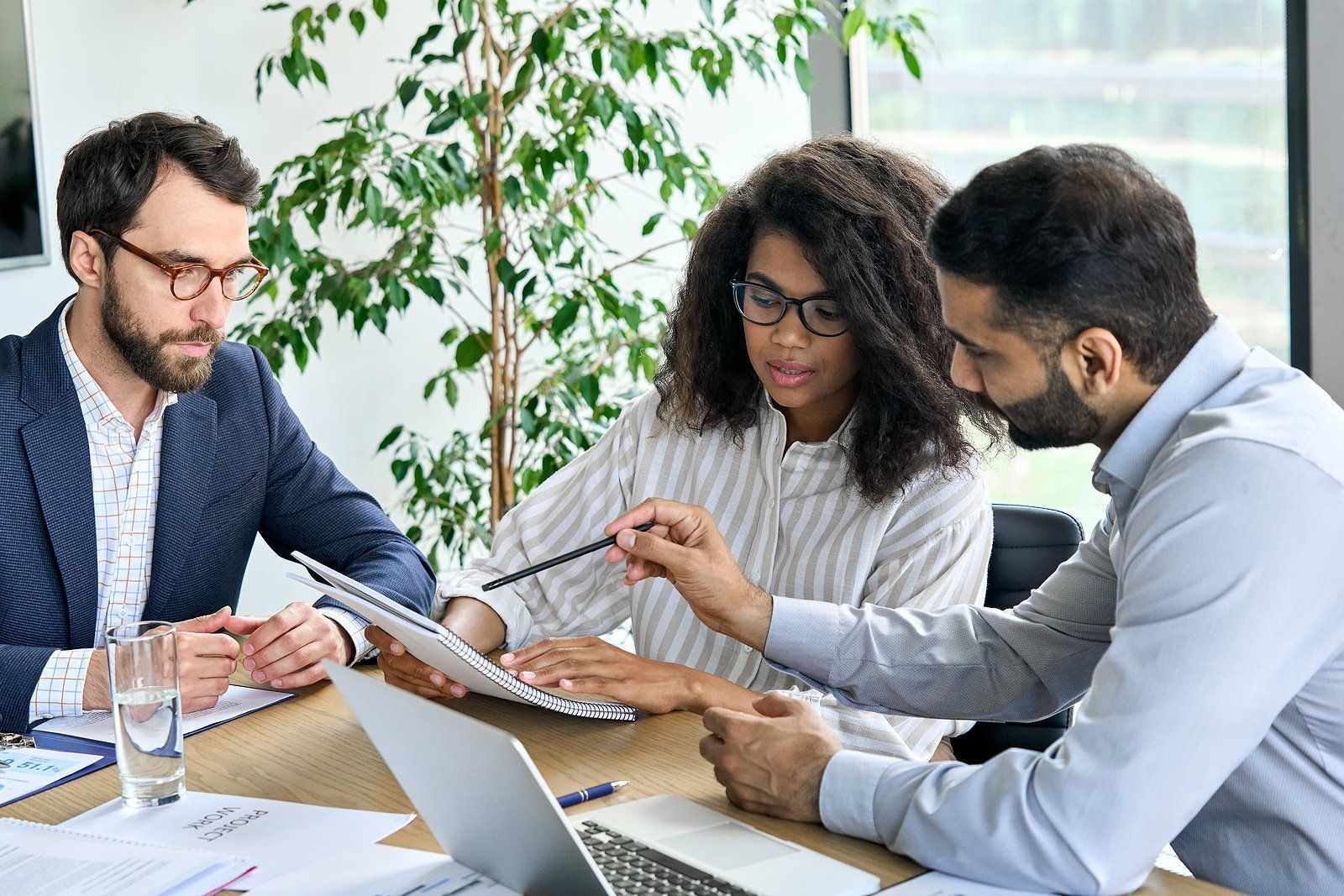 A group of people are sitting around a table looking at a laptop.