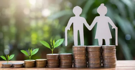 A paper cut out of an elderly couple standing on top of stacks of coins.