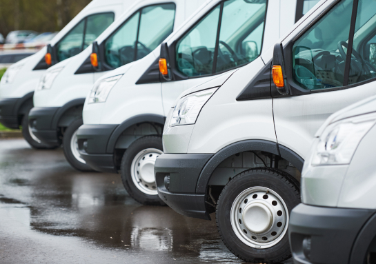 A row of white vans parked next to each other in a parking lot.