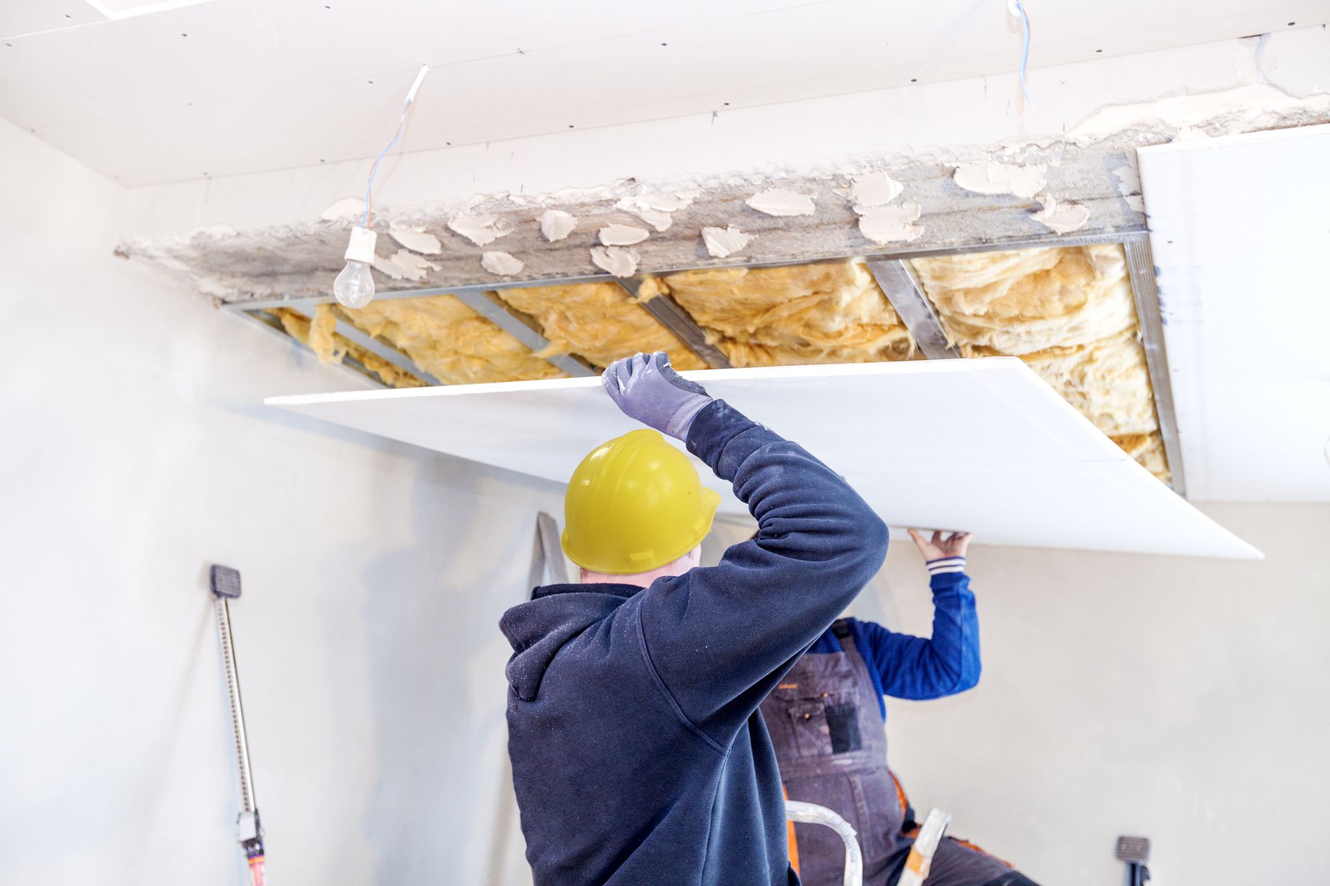 Two men are installing a ceiling in a room.