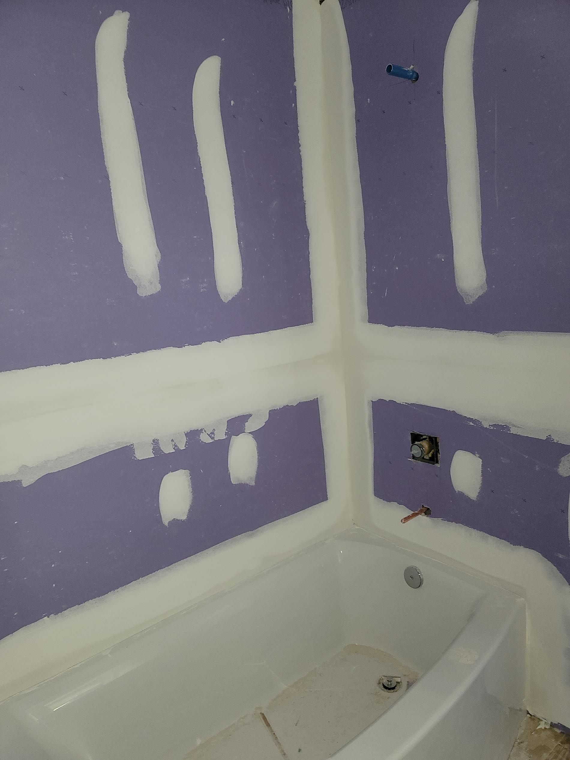 A bathroom with purple and white drywall and a bathtub.