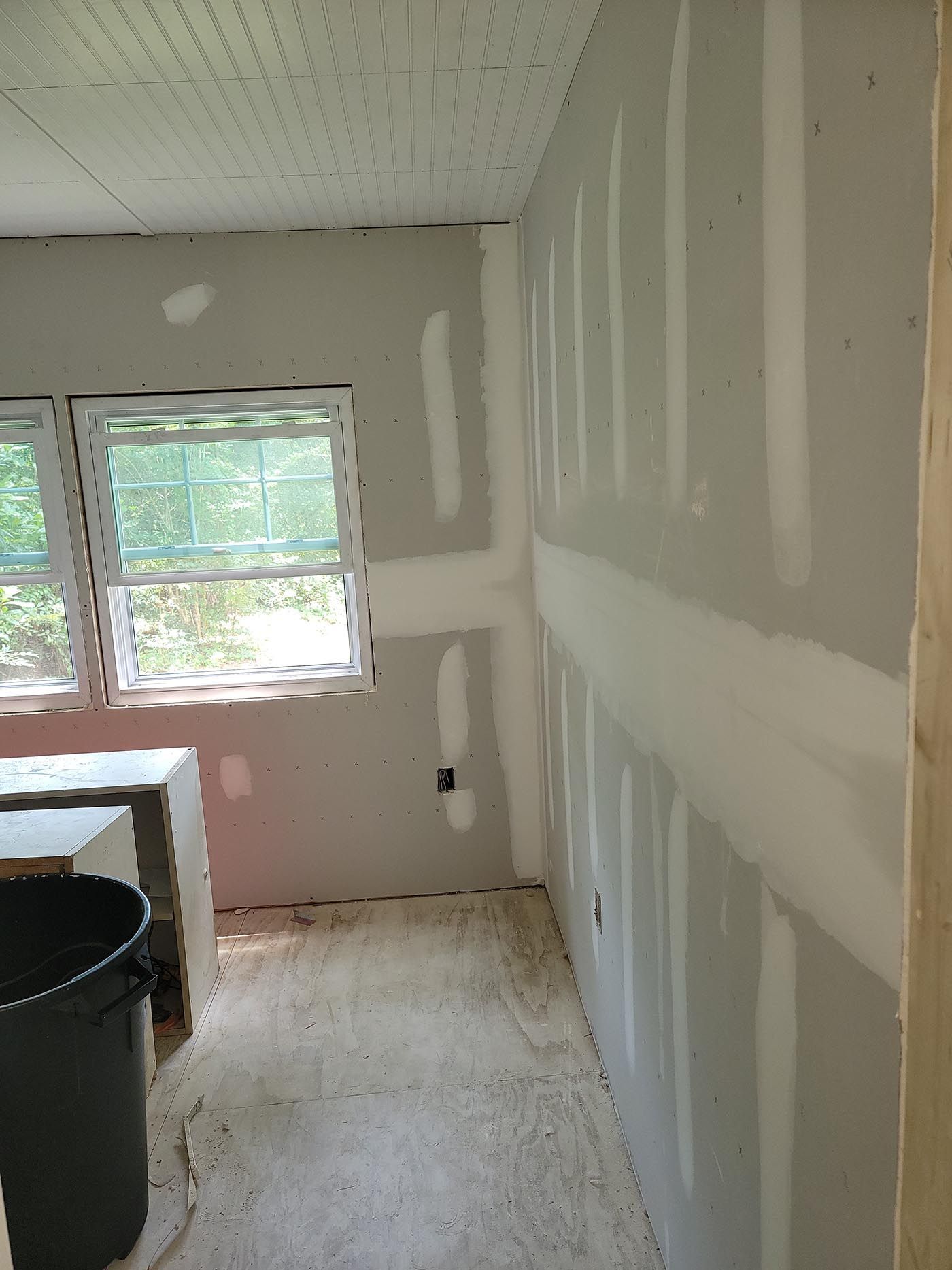 A corner of a room with drywall and a window