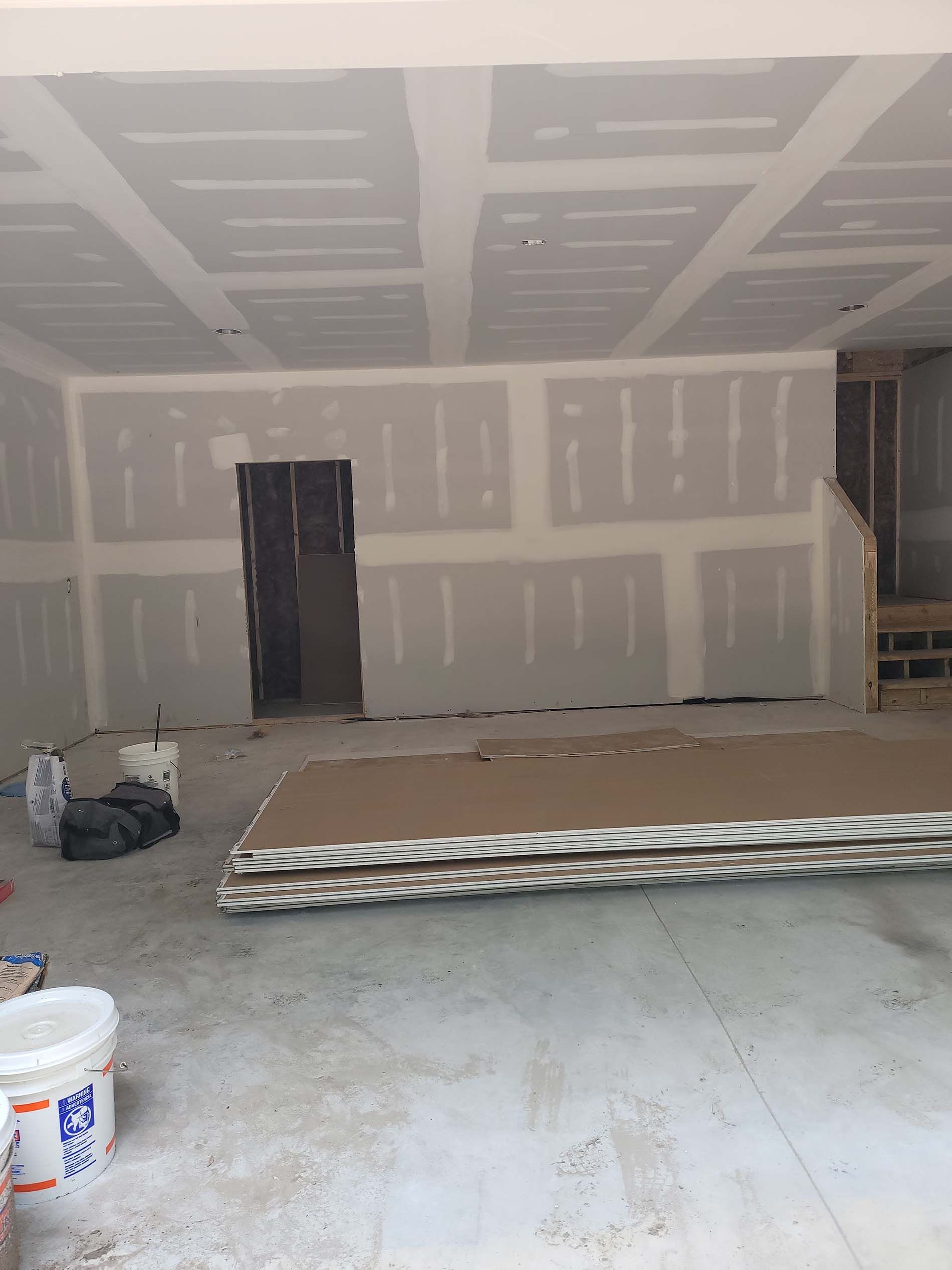 A room with a lot of drywall and a bucket of paint.