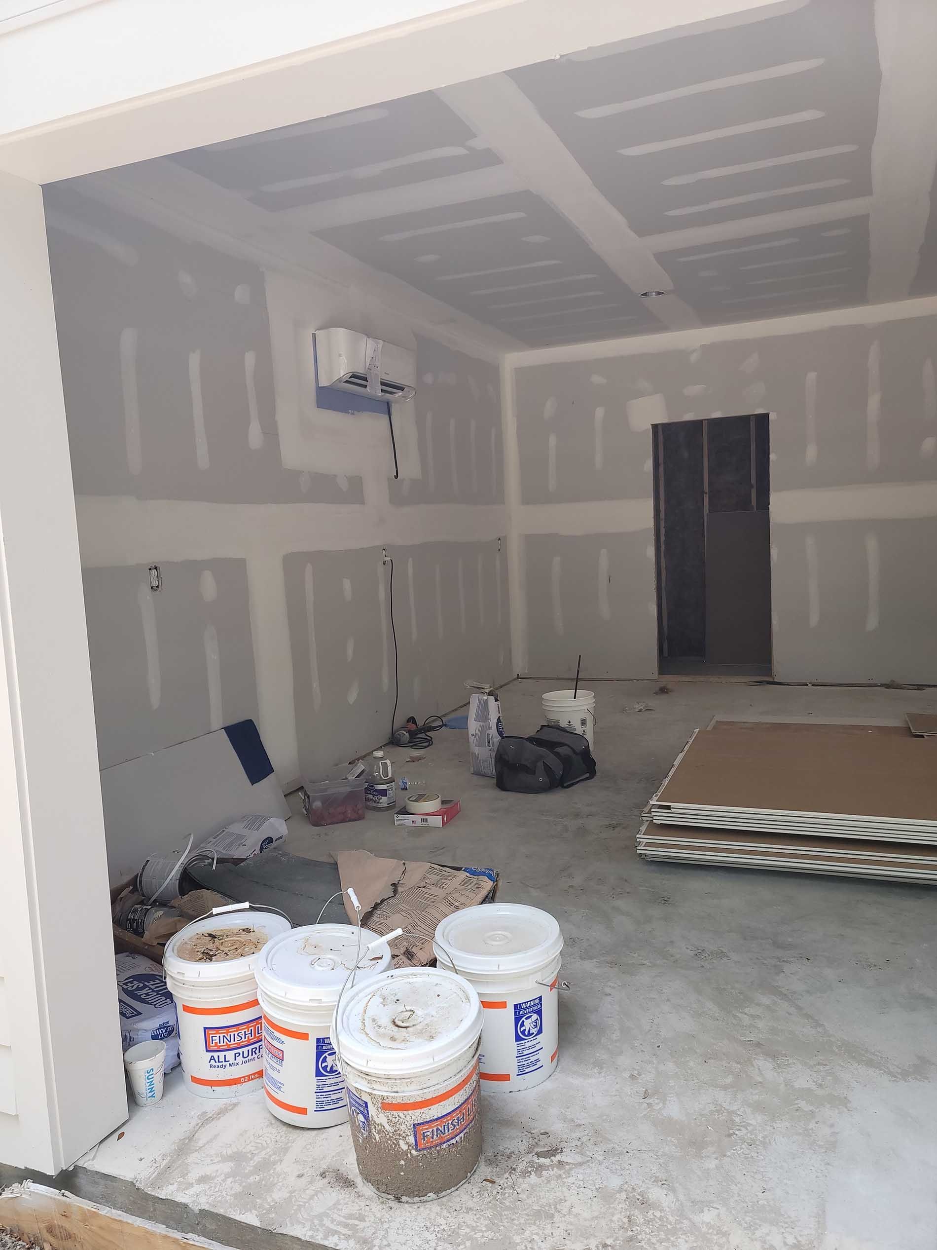 A garage under construction with buckets of paint on the floor.