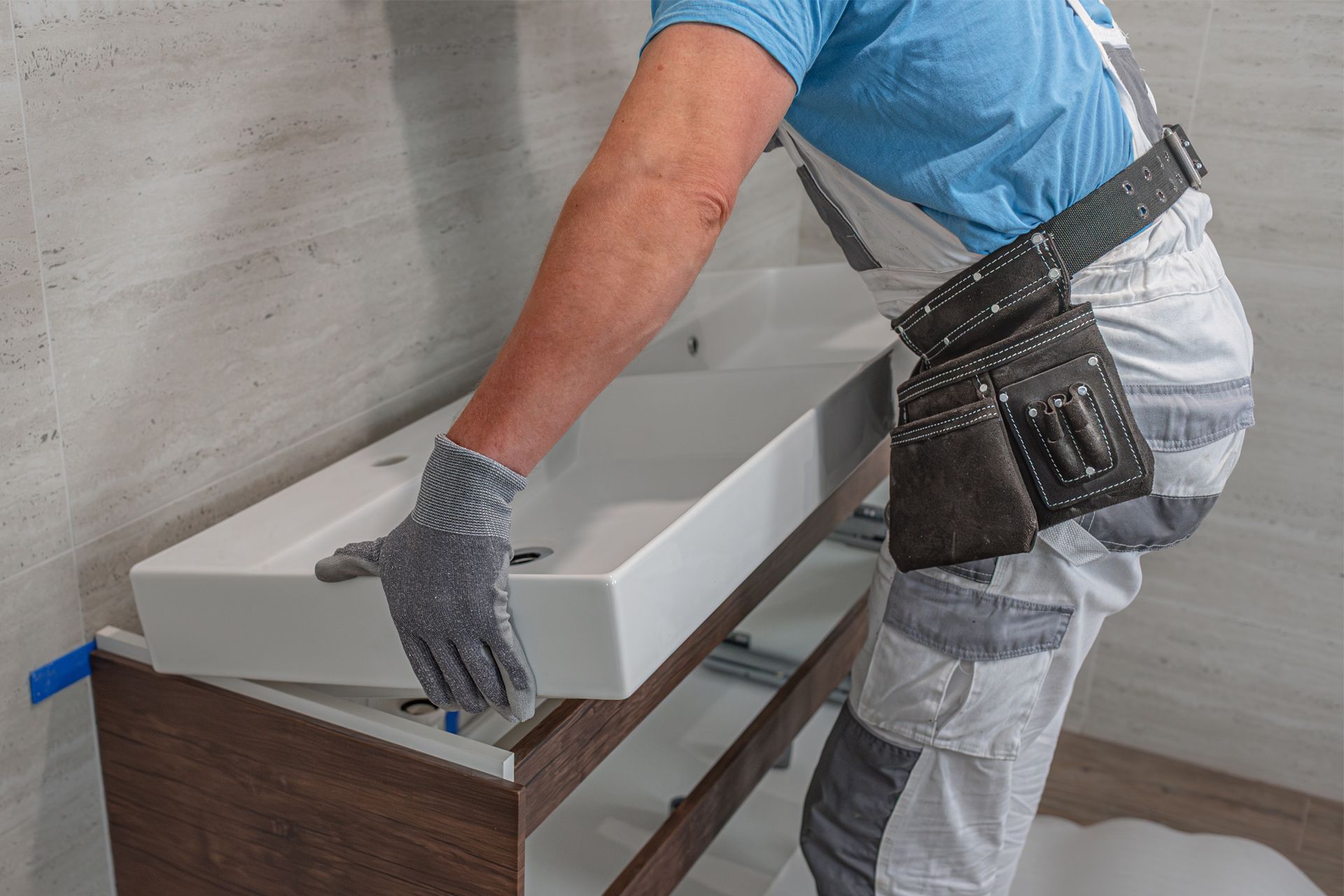 Person installs a white sink on a wooden cabinet in a bathroom.