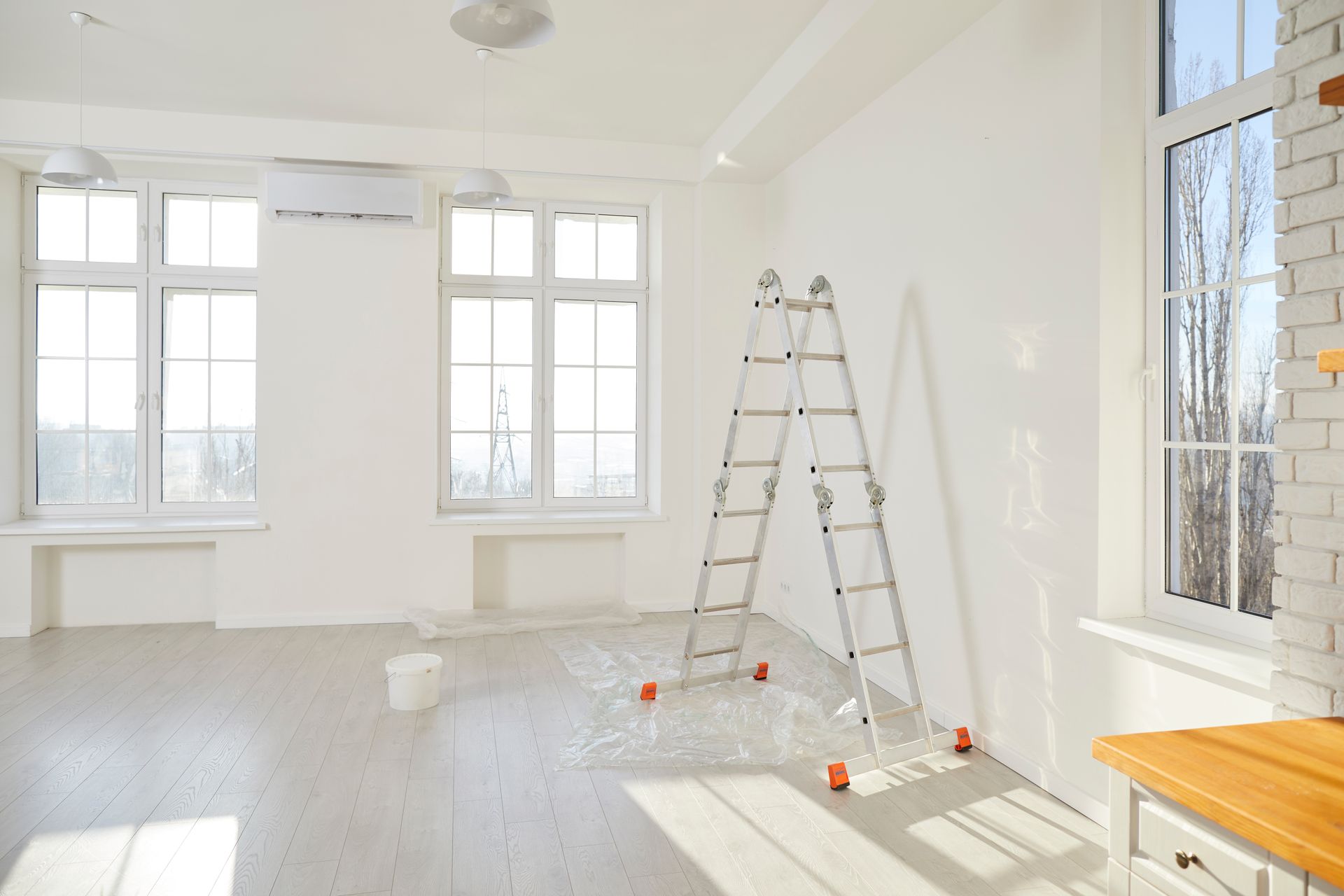 Bright room with ladder, two windows, white walls, and wooden floor. Sunlight streams in.