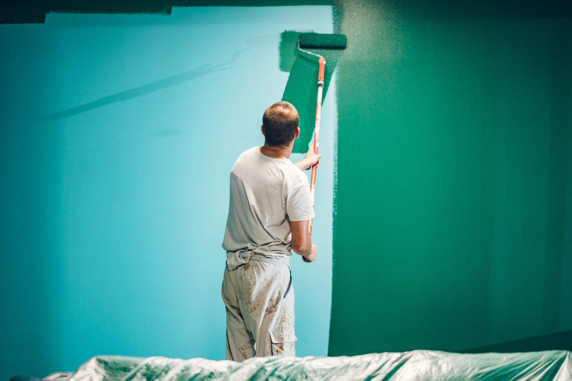 Person paints a wall green with a paint roller.