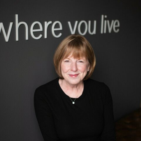 A woman is smiling in front of a sign that says where you live