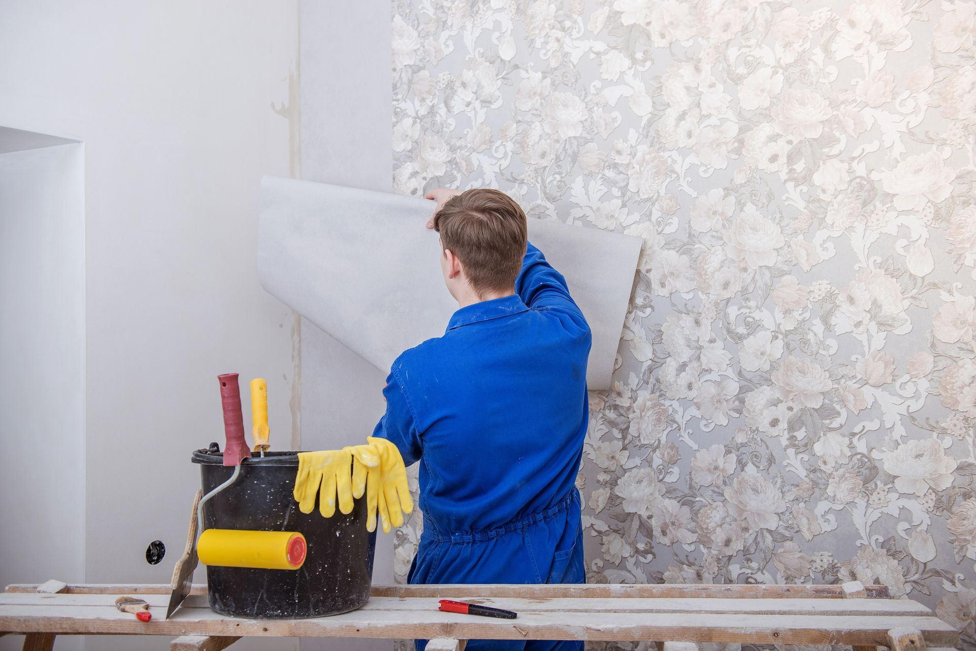 A young worker carefully wallpapering a wall in a room.