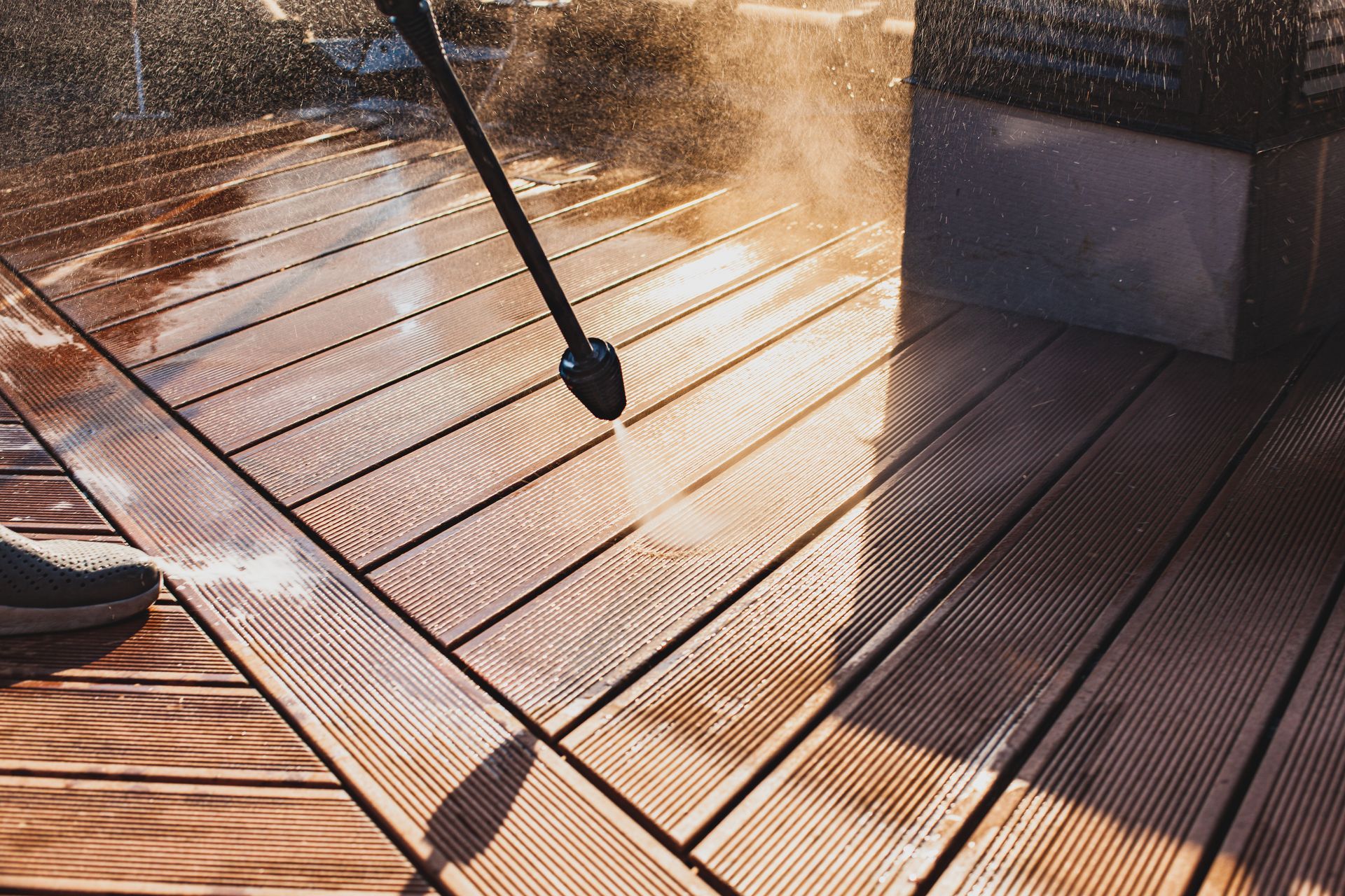 A man uses a power washer with high water pressure to clean a wooden terrace surface.