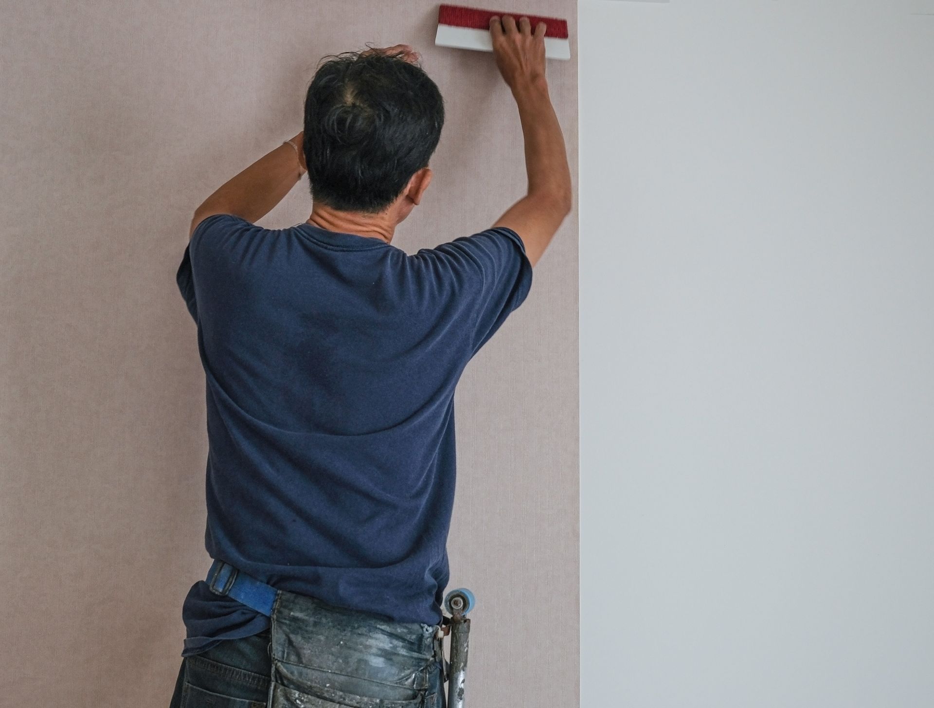 A worker is installing wallpaper on a white wall.
