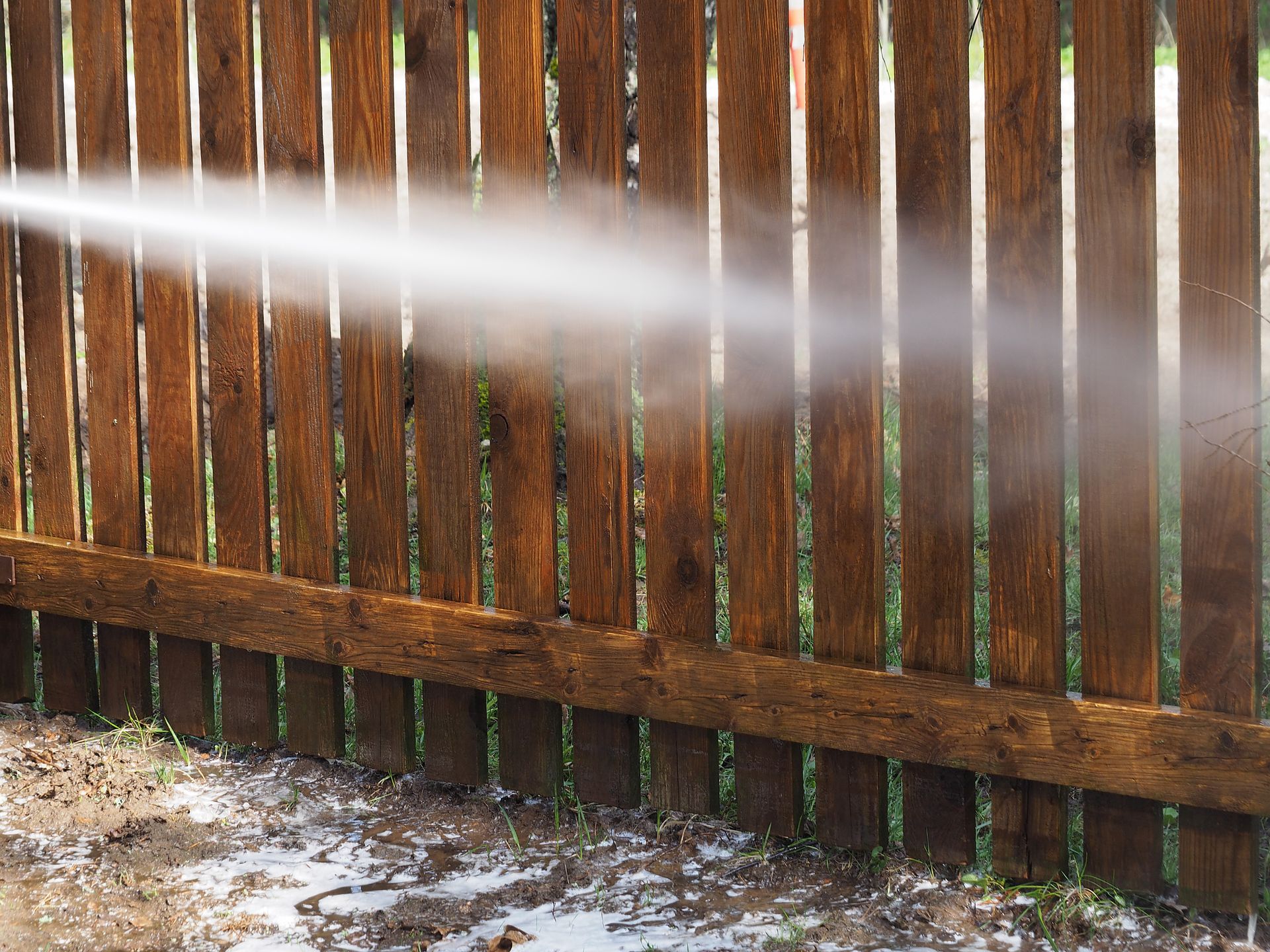 An individual power washes a wooden fence, removing dirt and grime, restoring its natural beauty.