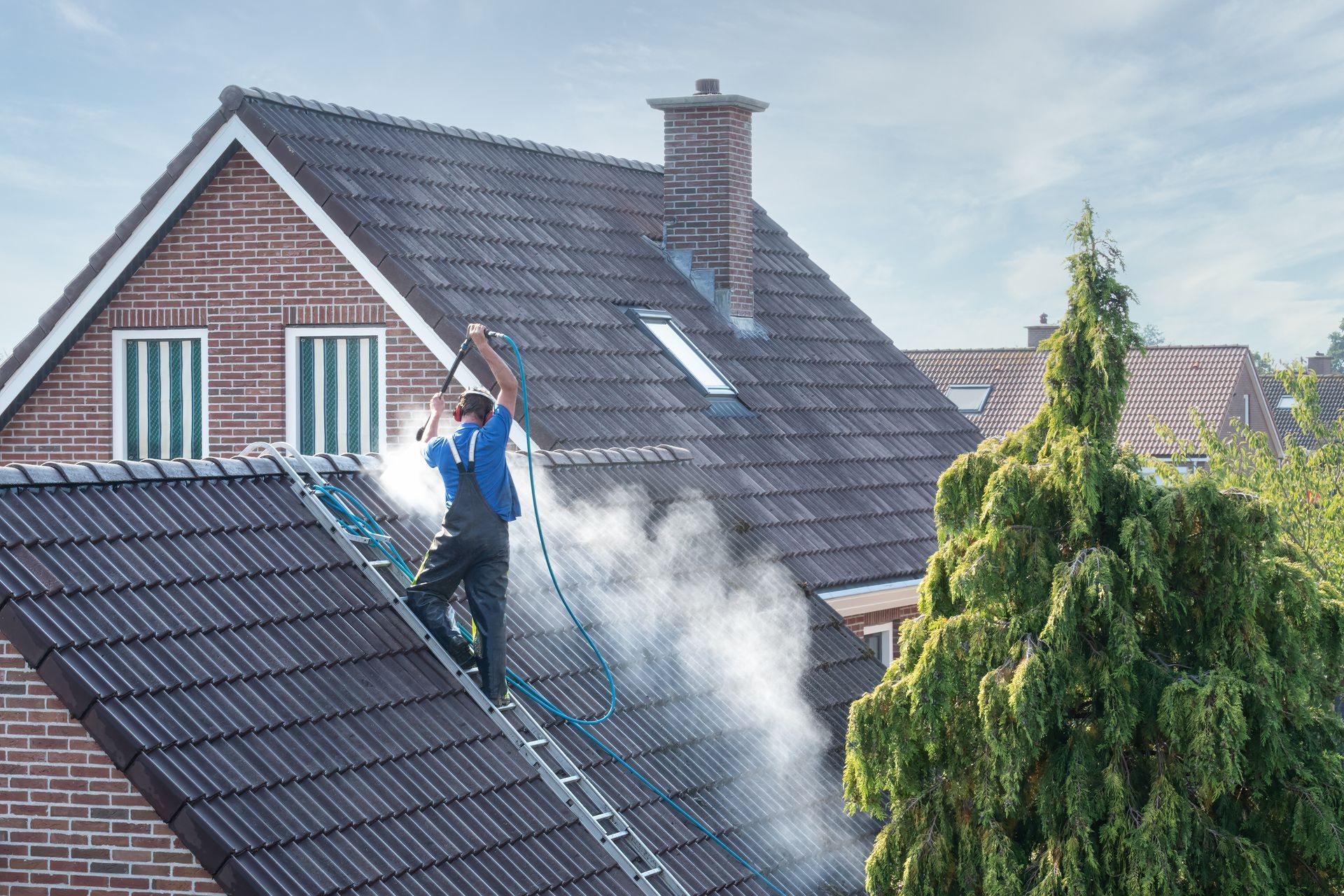 A person using a pressure washer to clean the roof tiles of a house during a soft washing process.