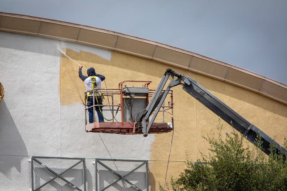 a man paints a building with a sprayer on a crane