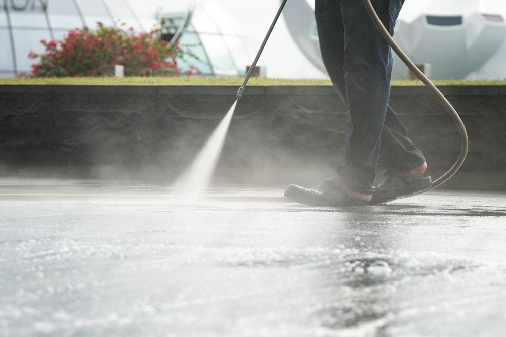 a person is using a high pressure washer to clean a concrete surface .