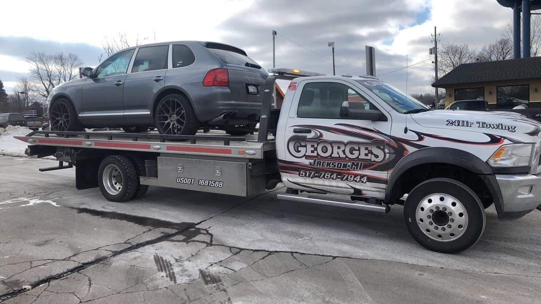 Gray SUV being towed on a flatbed truck by George's towing company on a snowy day.