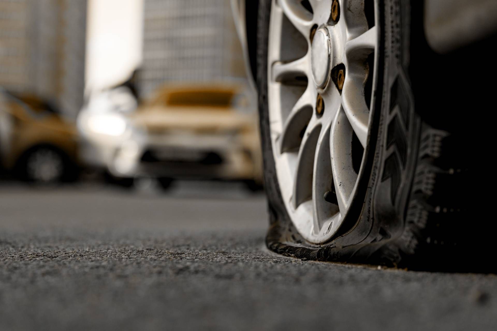 Close-up of a deflated car tire on asphalt road, cars blurred in background.