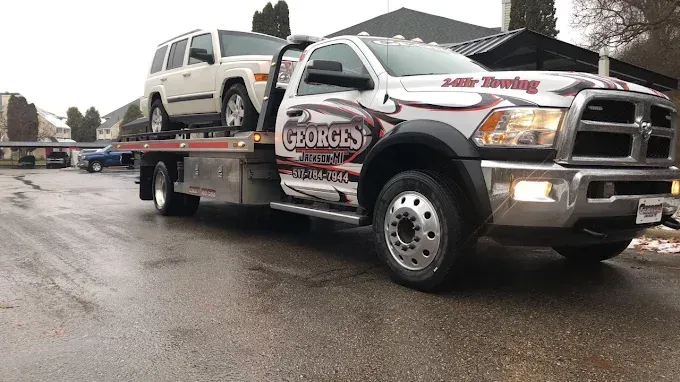 White Jeep loaded onto a George's Towing flatbed truck on a wet street.