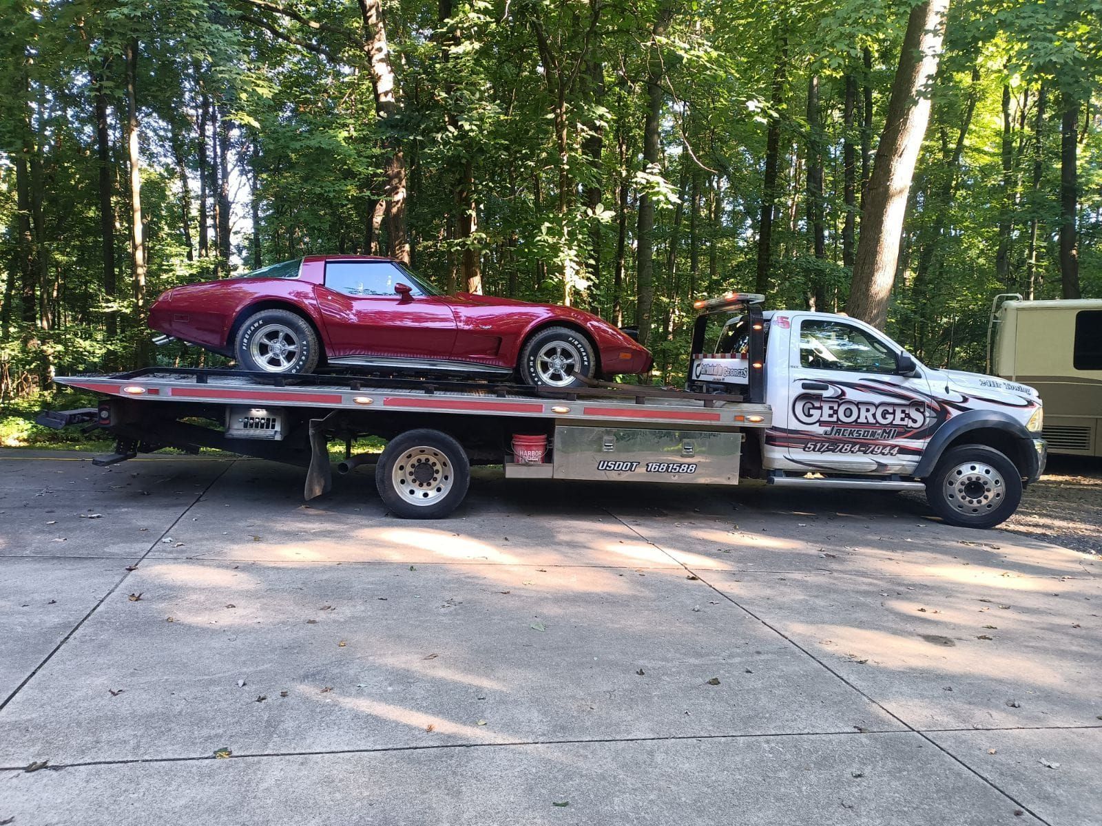 Red Corvette on a tow truck in a wooded setting; Georgia Towing logo visible.