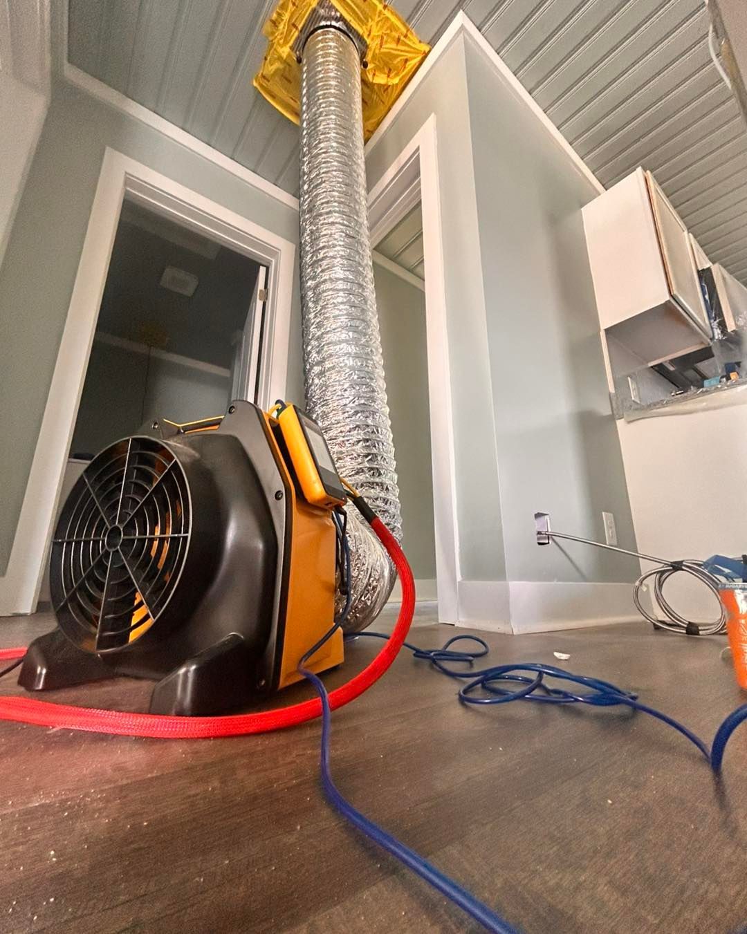 Fan with ducting for drying a room. The fan is black and yellow, connected to a flexible silver duct.