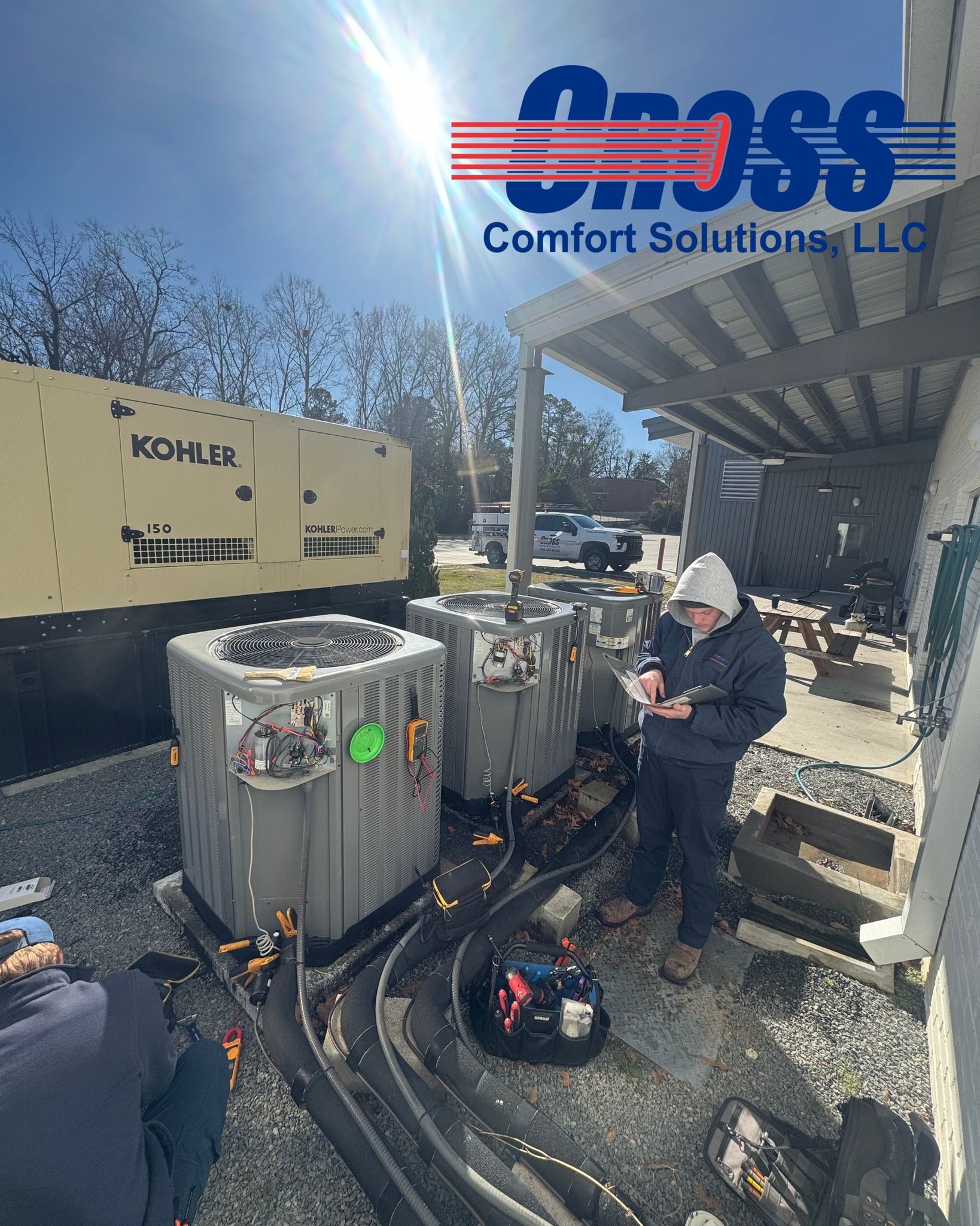HVAC technicians working on AC units near a generator on a sunny day. Cross Comfort Solutions logo present.