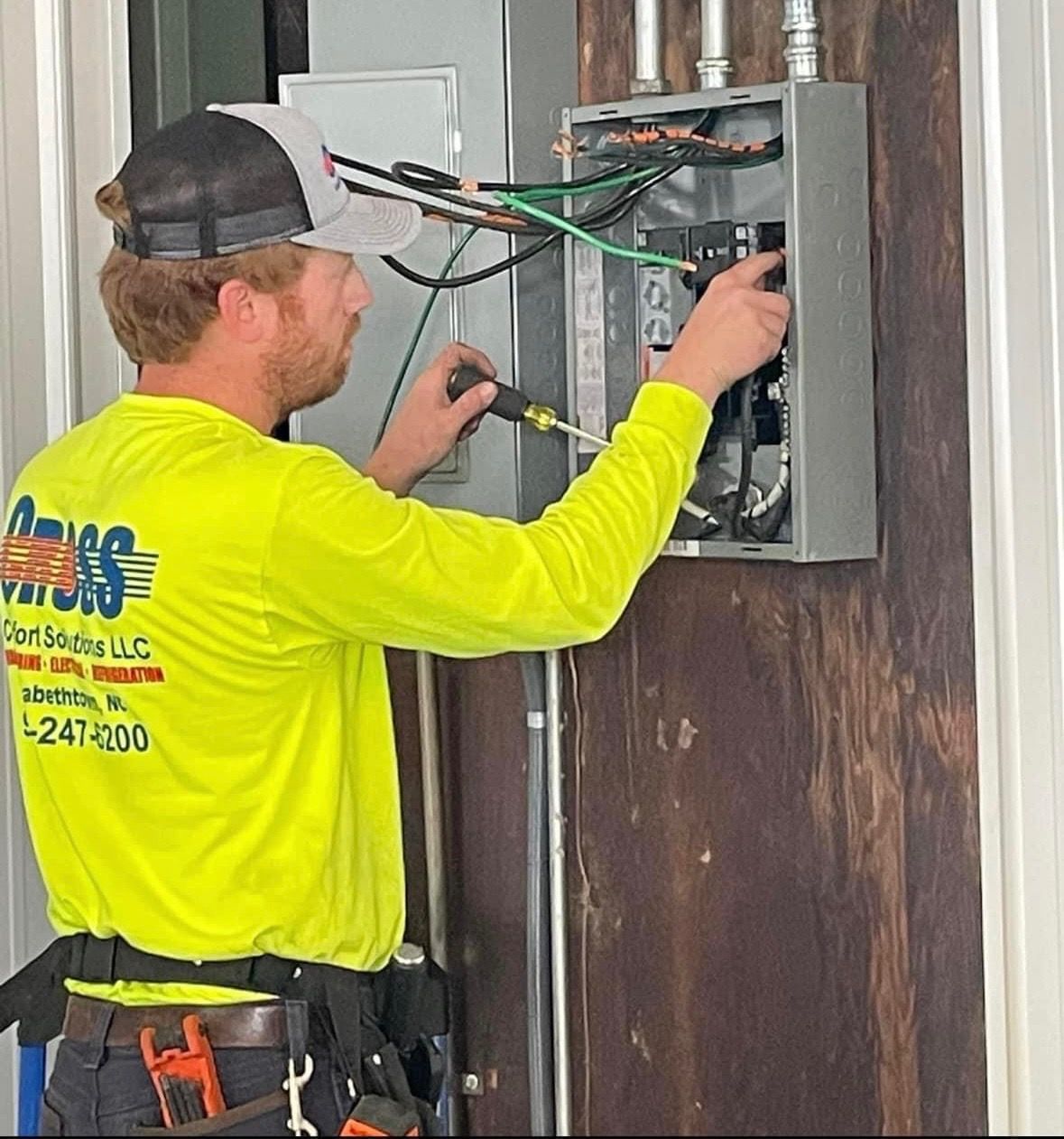 A man in a yellow shirt is working on a electrical box