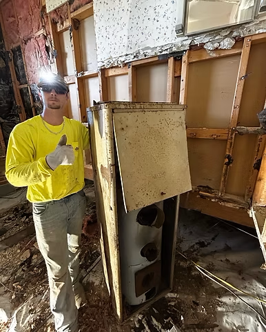 A man in a yellow shirt is standing next to a water heater.