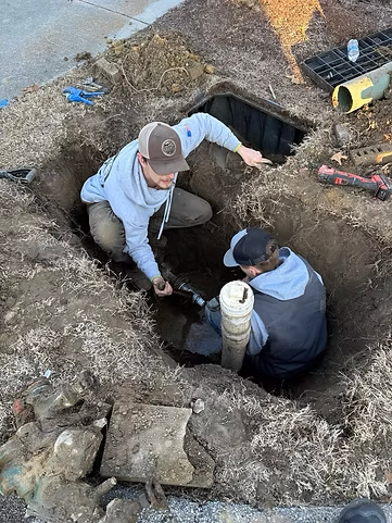 Two men are working in a hole in the ground.