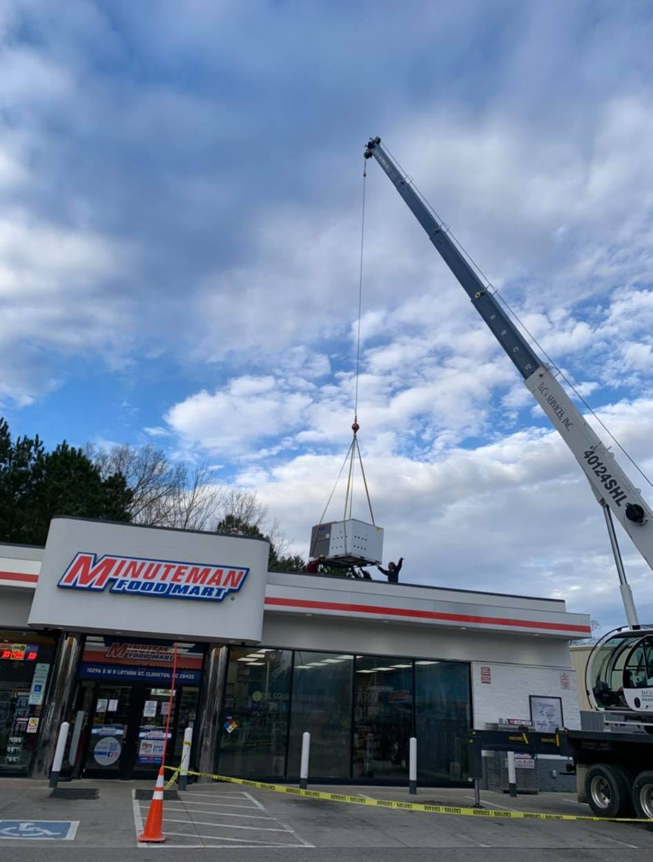 A crane is lifting a large box from the roof of a gas station.
