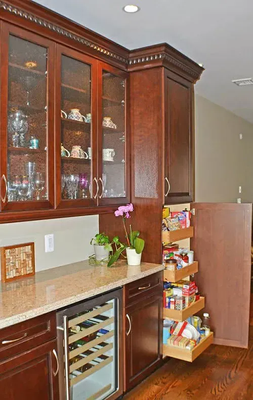 Kitchen corner: Dark wood cabinets, glass-front display, pull-out pantry, wine cooler. Beige countertop.