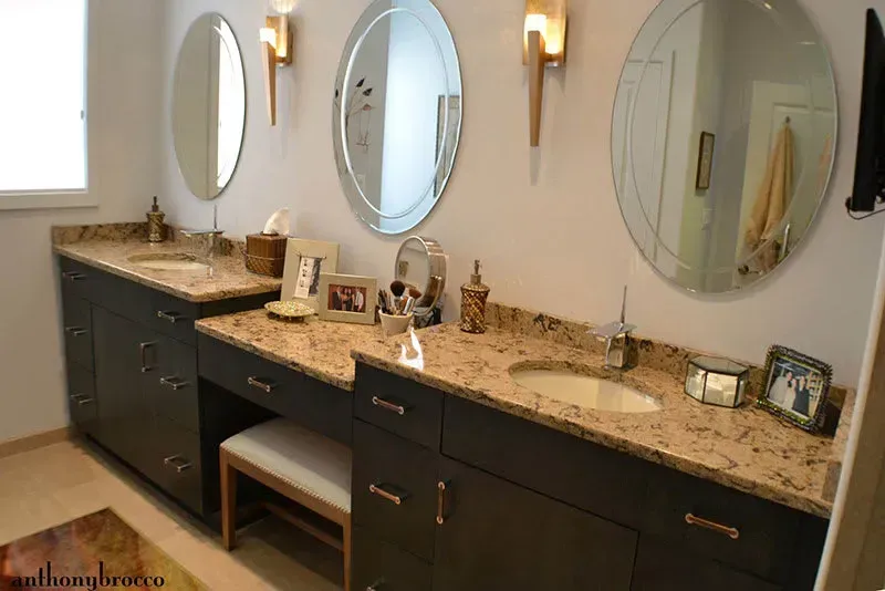Bathroom with brown cabinetry, toilet, oval mirror, and beige tile flooring.