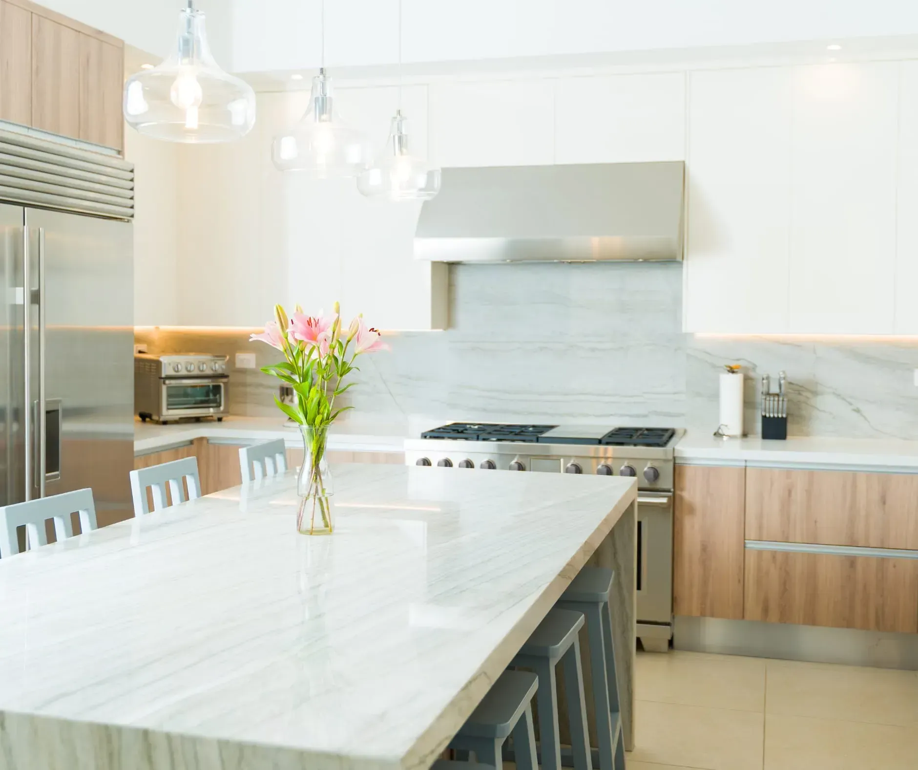 Modern kitchen with large island, stainless steel appliances, wood and white cabinets, and flowers.