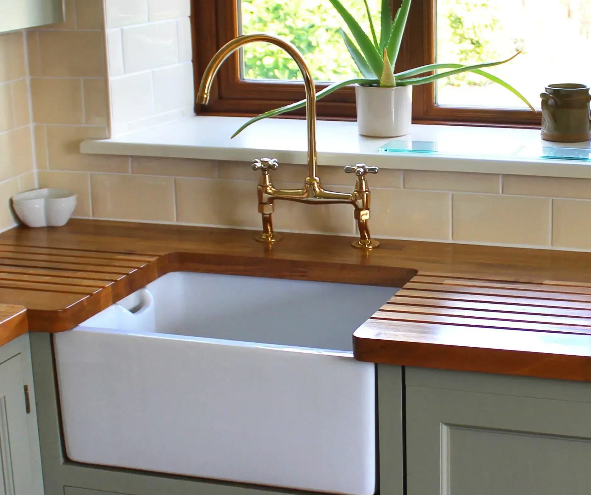 Kitchen sink with brass faucet, wooden countertops, and white subway tile backsplash.