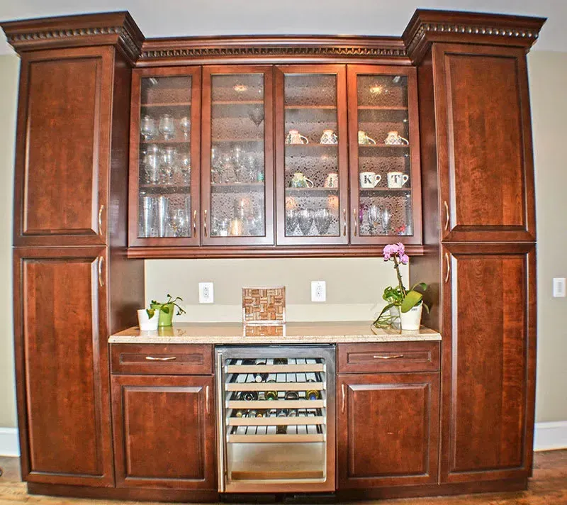 Dark wood kitchen cabinetry with glass-fronted cabinets, a wine fridge, and countertop space.
