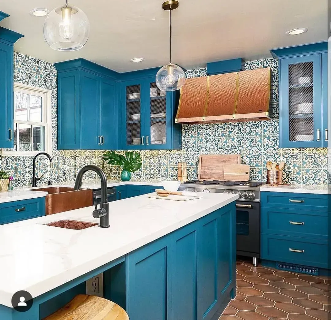 Bright blue kitchen with white countertops, copper sink, and patterned tile backsplash.