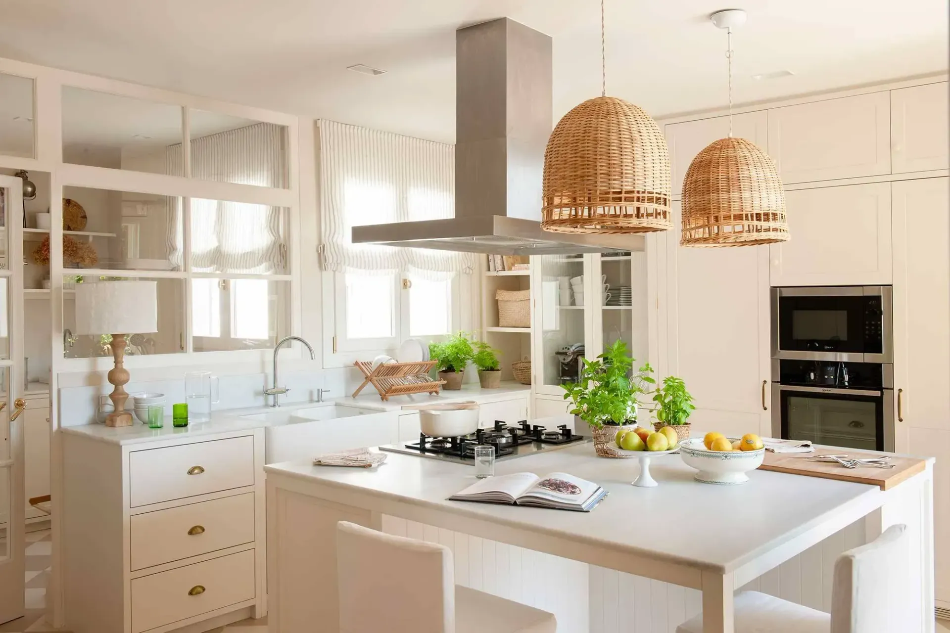 Bright white kitchen with island, stove, and woven pendant lights.