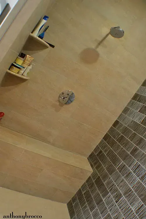 Shower interior with built-in bench and shelves. Beige tile on walls, brown mosaic tile accents, chrome fixtures.