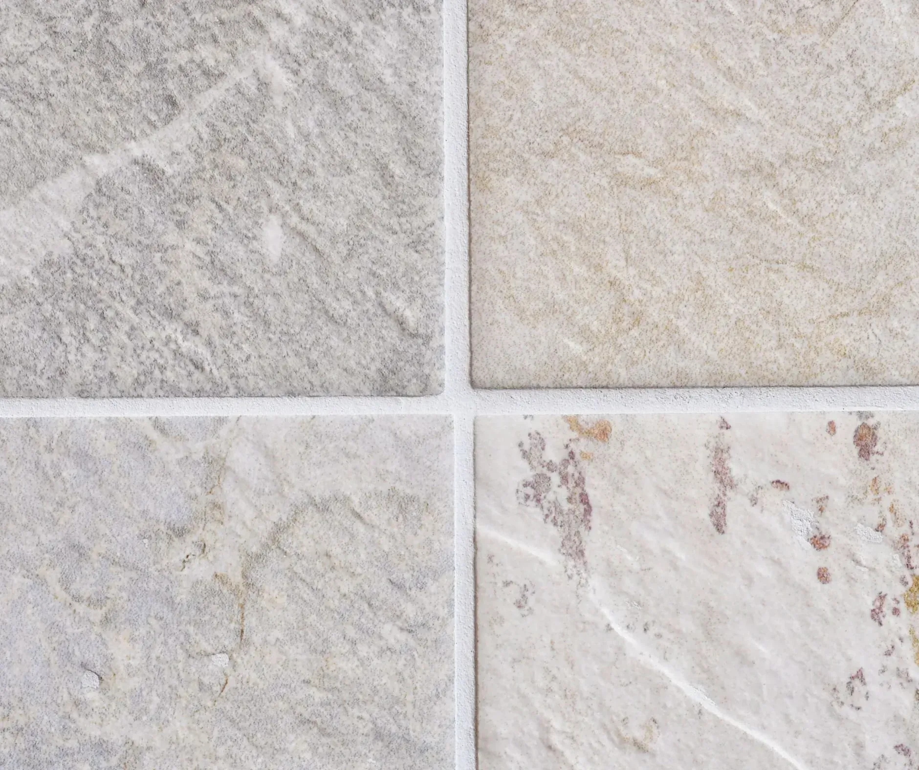 Four light-colored tiles with varying textures and shades of gray, beige, and off-white, separated by white grout lines.