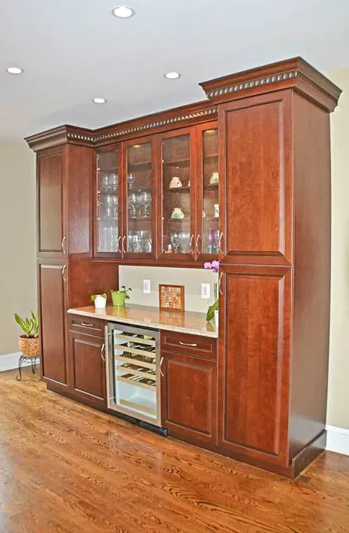 Dark wood home bar with wine fridge, glass-front cabinets, and marble countertop.