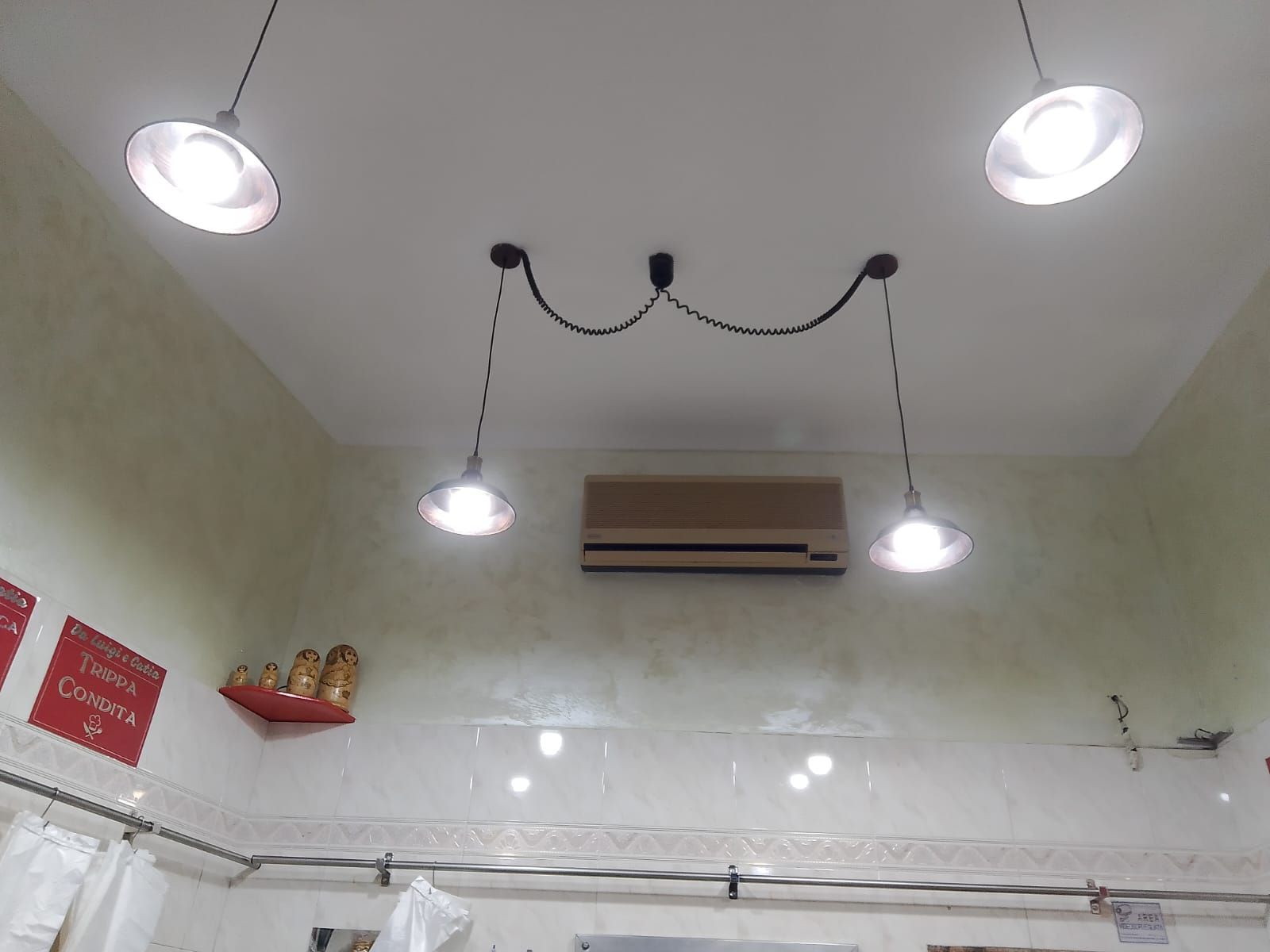 Quattro lampade a sospensione pendono da un soffitto bianco, sopra un condizionatore.