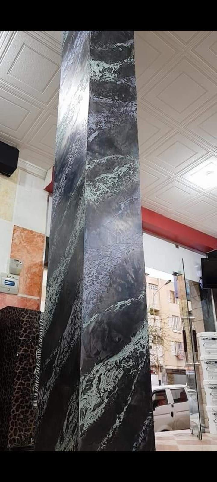 In una stanza si erge un alto pilastro rettangolare con un motivo marmorizzato scuro.