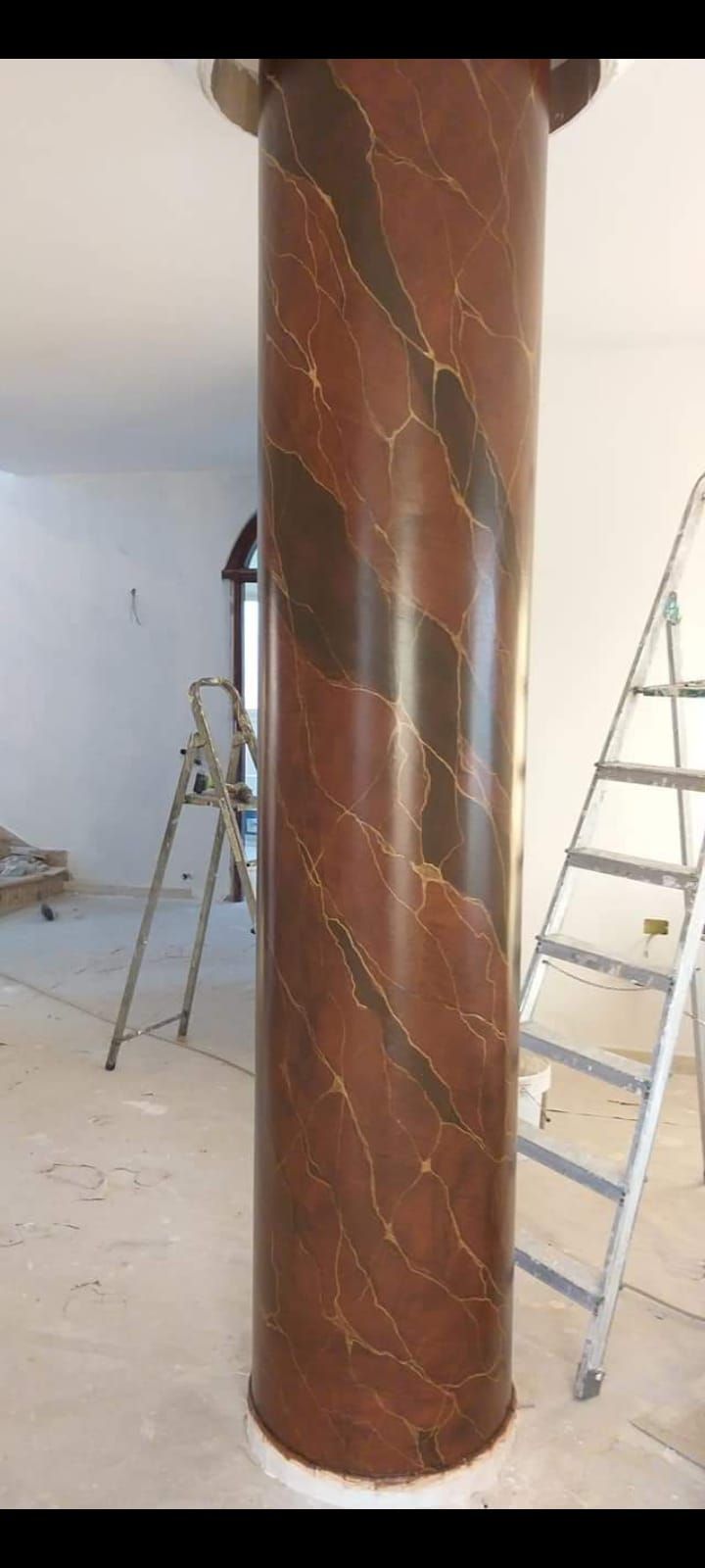 Una grande colonna di marmo marrone con striature scure. Due scale si trovano ai lati della colonna.