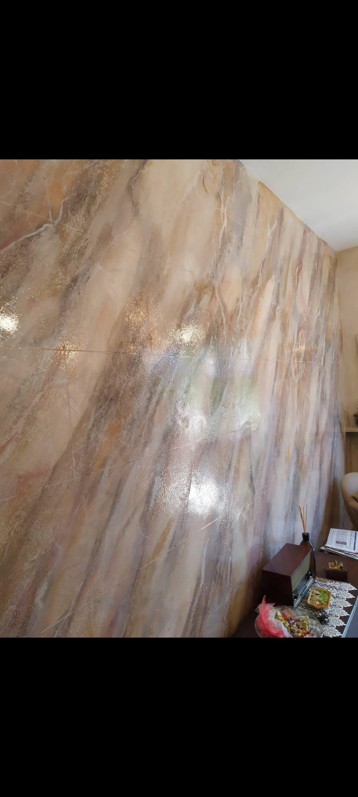 Parete con motivi in marmo e punti riflettenti; accenni di mobili e un piano di lavoro.